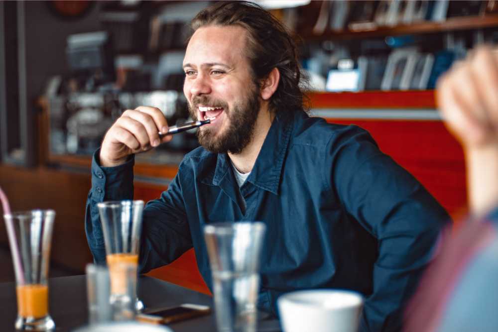 happy bearded man vaping at a restaurant