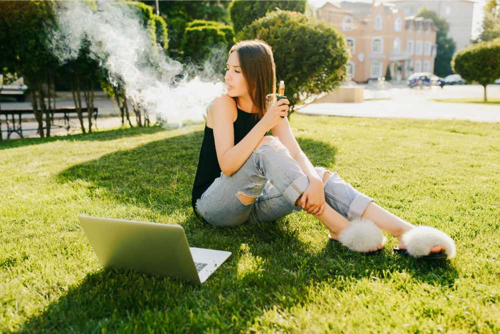 woman vaping on lawn with laptop