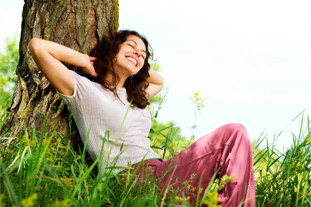 happy woman relaxing outside next to tree