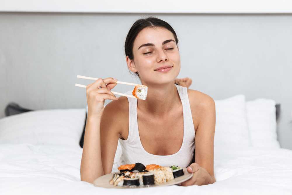 woman relaxing eating sushi in bed